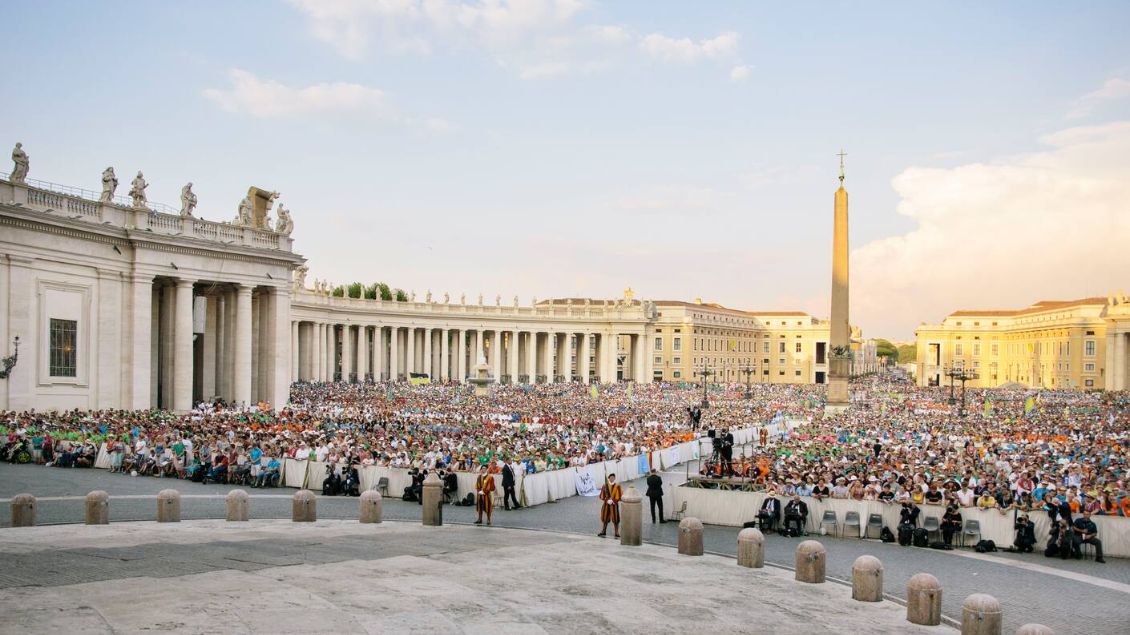 Der Petersplatz mit vielen Menschen in orangenem Sonnenlicht.