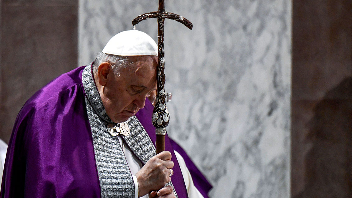 Papst Franziskus im violetten Chormantel an ein Kreuz gelehnt