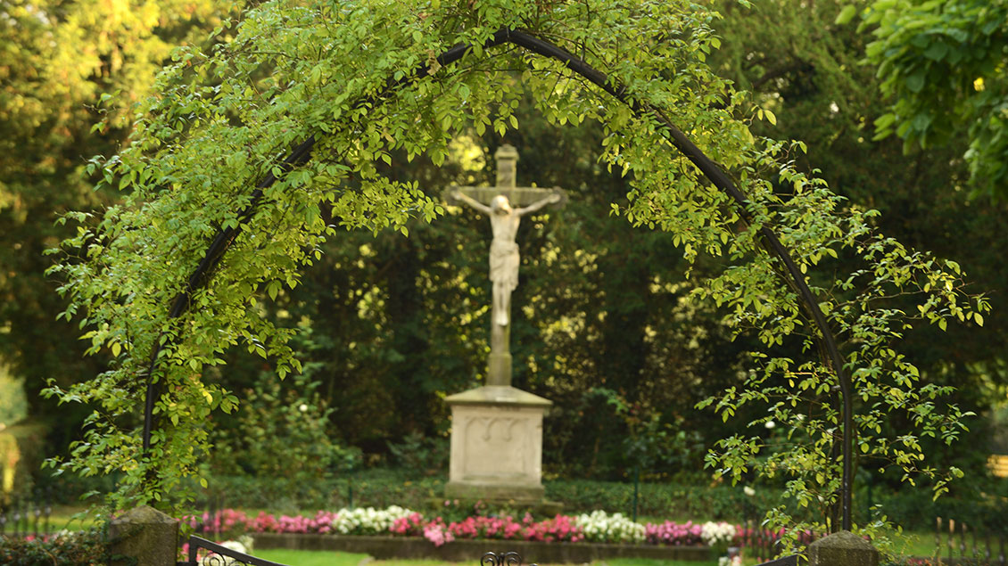 Eingang zu einem Friedhof mit einem Kreuz im Hintergrund