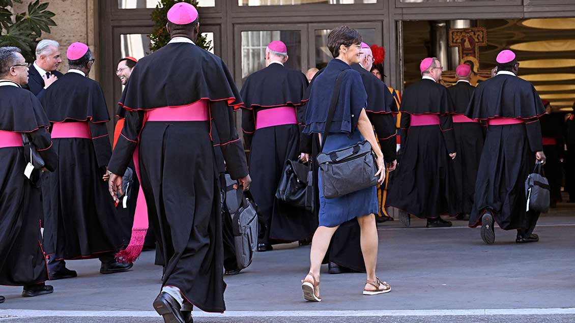 Eine Frau und mehrere Bischöfe betreten Audienzhalle in Rom 