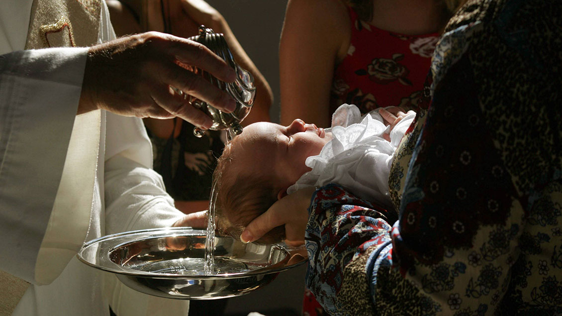 Pfarrer begießt Kopf eines Kindes bei Taufe mit Weihwasser